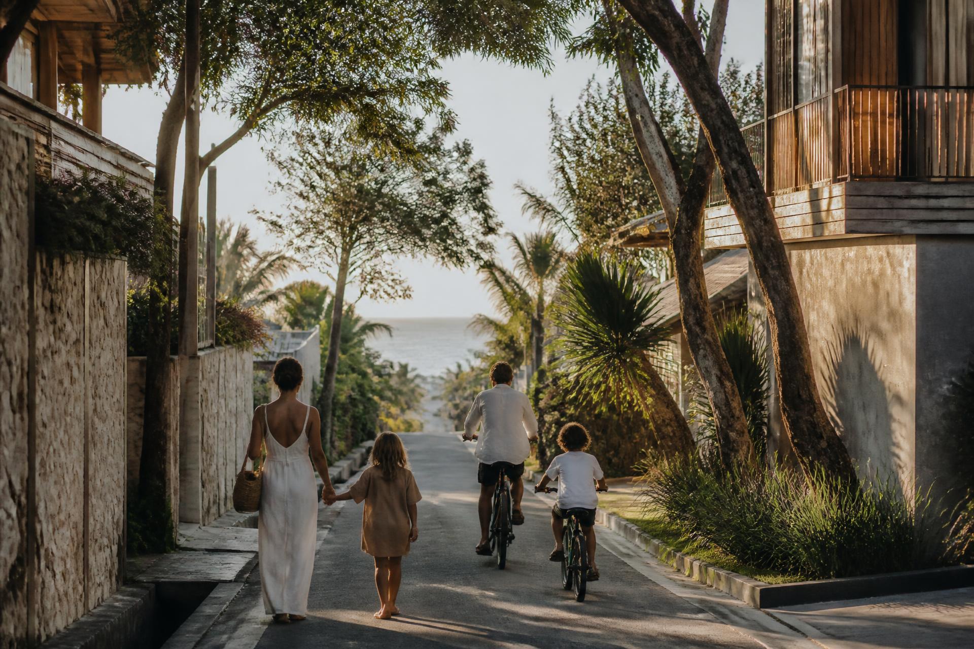 A family walking and cycling towards the beach in a quiet Bali neighbourhood